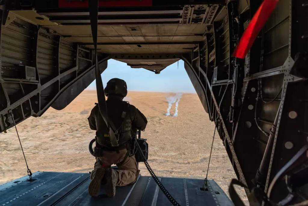 Soldat sitzt am offenen Heck eines Militärhubschraubers und blickt über Wüstengelände