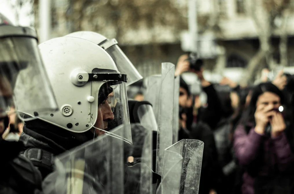 Polizisten mit Schutzhelm und Visier im Einsatz vor Schaulustigen