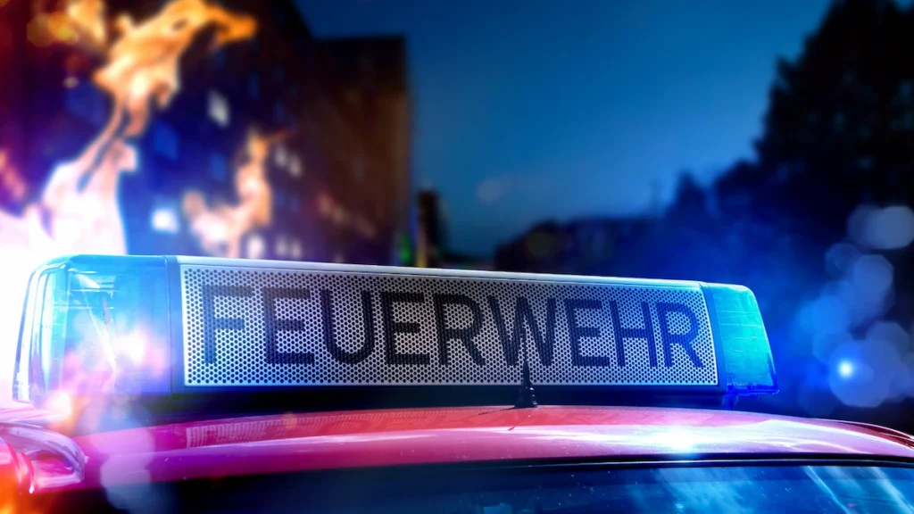 Blaulicht eines Feuerwehrfahrzeugs vor einem brennenden Gebäude bei Nacht
